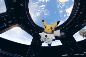 Űrhajósruhás Pikachu plüssfigura a Nemzetközi Űrállomás Cupola ablakában, mögötte a Föld
