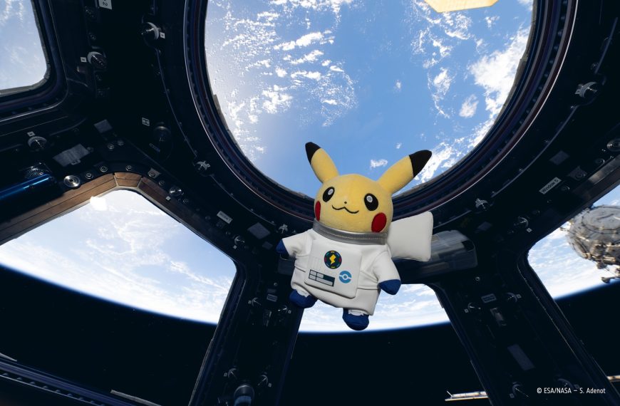 Űrhajósruhás Pikachu plüssfigura a Nemzetközi Űrállomás Cupola ablakában, mögötte a Föld